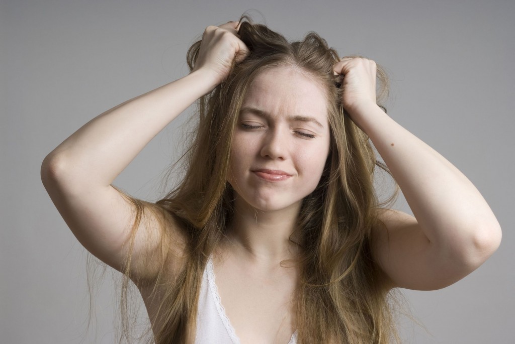 young woman eyes closed with Tourettes with her hand over her head pulling her hair.