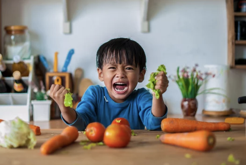 Child throwing tantrum squeezing vegetables