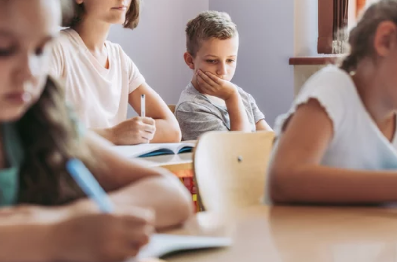 Depress young boy sitting in classroom distracted.