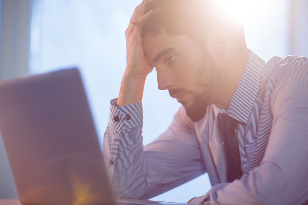 Man stressed with his hand on his head sitting looking at laptop.