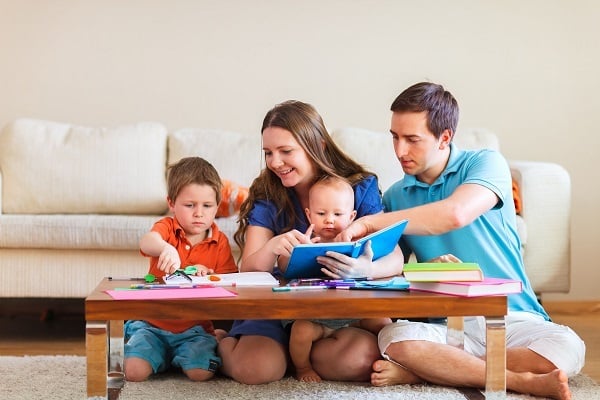 Parentings with children helping them improve their behavior. young child is doing homework, Mother is reading to toddler, father beside her.