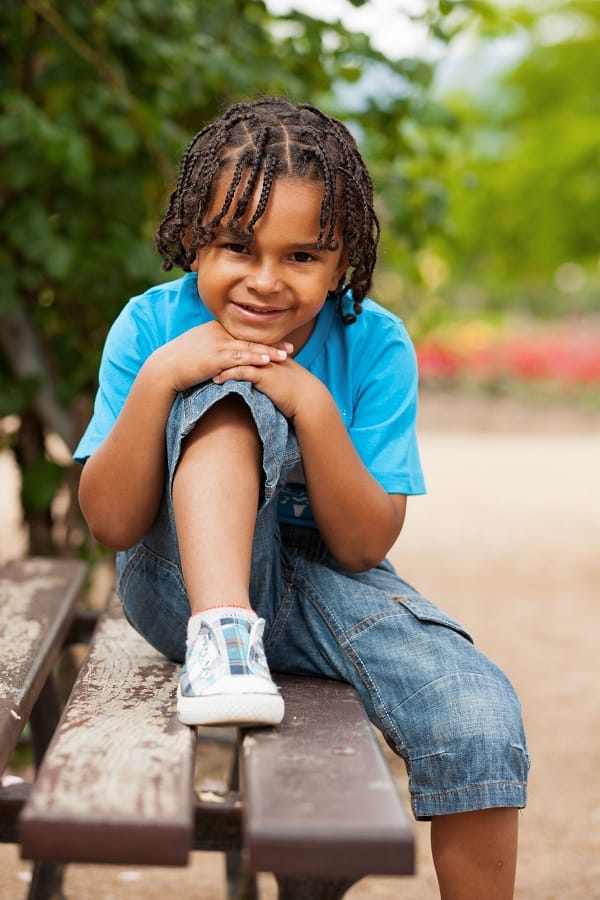 Young boy sitting on park bench smiling. 